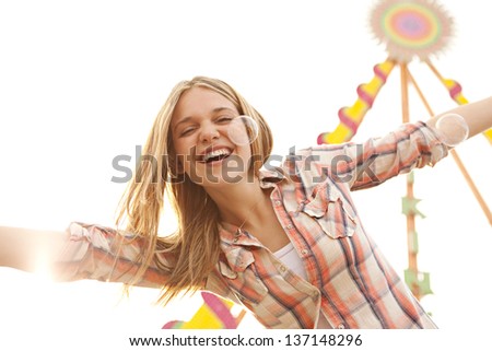 Close up portrait of a young attractive teenage girl in a colorful attractions park arcade, playing with bubbles, with her arms outstretched up in the air.