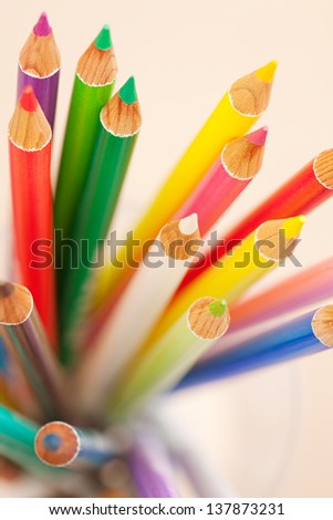 Close up detail of a bunch of colored school art pencils pointing upwards, isolated on a plain background.