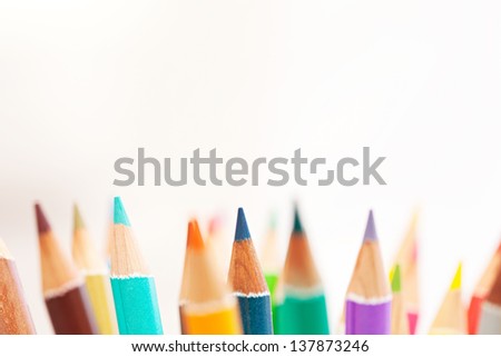 Close up detail of the tips of a bunch of colored school art pencils pointing upwards, isolated on a white background.