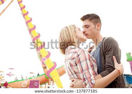 Close up side view portrait of a young couple kissing while visiting a fun fair park arcade against the sky.