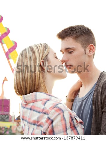 Close up portrait of a young couple kissing while visiting an amusement park arcade with the sun shining in the sky.
