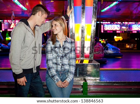 Attractive young couple visiting an amusement park arcade standing by a bouncy cars ride, talking and having fun during an exciting night out.