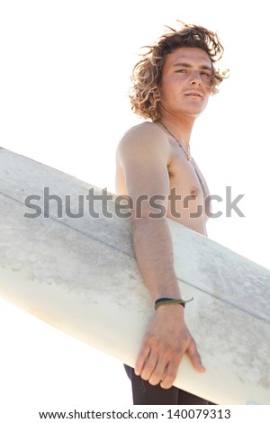 Close up portrait of a young surfer sports man standing on a beach while wearing a neoprene rubber surfing suit, being thoughtful and holding a surfing board during a sunny day.