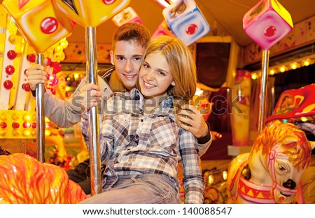 Young joyful couple visiting an attractions park and hugging while enjoying a carousel ride during a fun night out together.