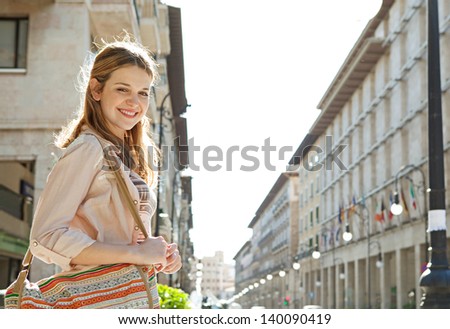 Side portrait of a young teenage girl walking in a city street during a sunny day with large buildings forming a perspective in the background.