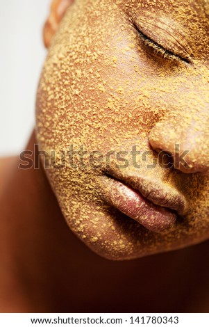 Close up beauty portrait of a young african american black girl half face with yellow cosmetic powder covering her face, with her eyes closed.