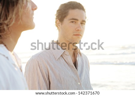 Portrait of two young men friends hanging around together on a golden beach on vacation, relaxing during a summer sunset.