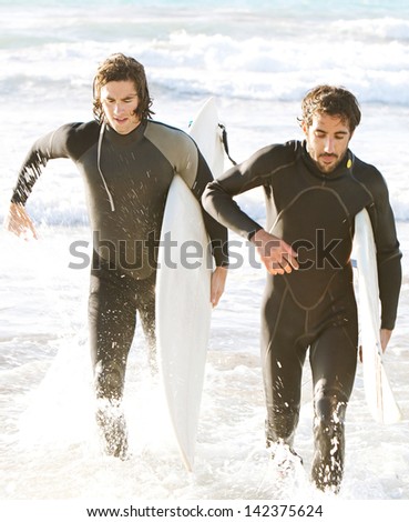 Two young sports surfer men running back to shore with their surfing boards while surfing together on a sunny day during a summer vacation.