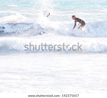 Two sports surfer men starting to ride a wave, one standing up on his board and the other falling down into the sea, leaving a flying surfing board and splashing water during a summer day on vacation.