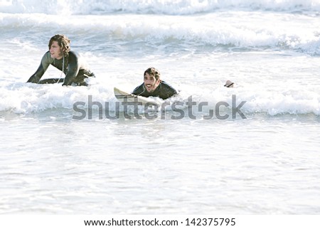 Two young sports surfer men swimming back and relaxing on their surfing boards while surfing together on a sunny day during a summer vacation.