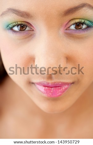 Close up beauty portrait of a young girl face with voluptuous lips wearing a rainbow color eye shadow and smiling with glossy pink lipstick.
