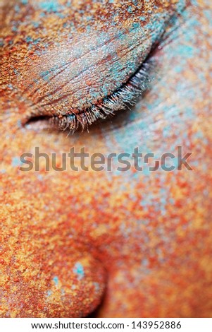 Close up beauty portrait of a young girl face and closed eye wearing golden yellow, red and blue and make up powder pigment covering her face, detail texture view.