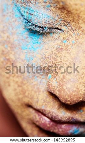 Close up beauty part portrait of a young girl face with voluptuous lips wearing golden yellow and blue and make up powder pigment covering her face, detail texture view.