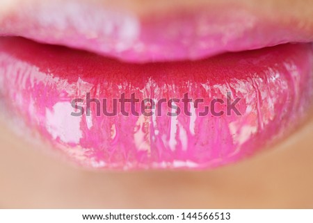Close up beauty detail view of a young woman\'s mouth with perfect lips wearing bright pink glossy lipstick, macro view.