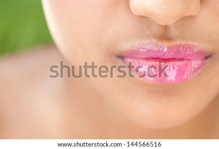 Close up detail view of a beautiful young woman\'s mouth with perfect lips wearing glossy pink lipstick against a nature green background.