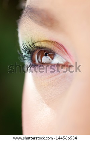 Close up detail view of a young woman\'s open eye, looking away from camera and wearing a rainbow eyeshadow and make up.