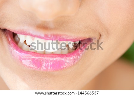 Close up detail view of a young african american woman\'s mouth wearing glossy pink lipstick and smiling showing white clean teeth.