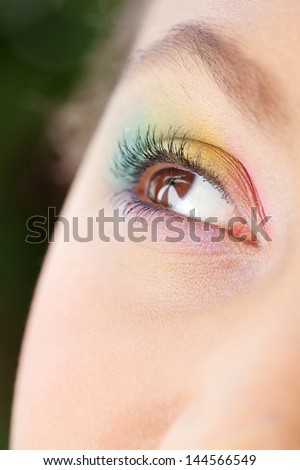 Close up detail view of an african american young woman\'s open eye, looking up and away from camera and wearing a rainbow eyeshadow and make up.