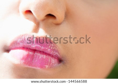 Close up detail view of a beautiful young woman\'s mouth with perfect lips wearing glossy pink lipstick during a sunny day.
