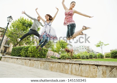 Group of three friends jumping up in the air together while visiting an urban park in the city, having fun and enjoying the energy during a summer day on vacation.