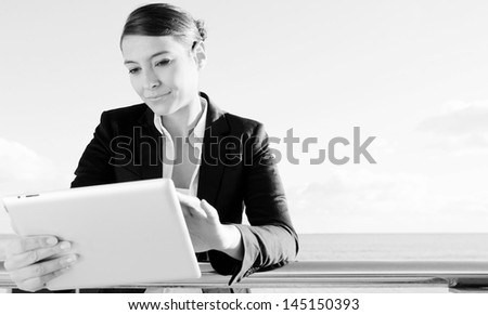 Black and white close up portrait of an attractive professional business woman using a digital tablet and touching the screen while wearing a suit against a sky background.