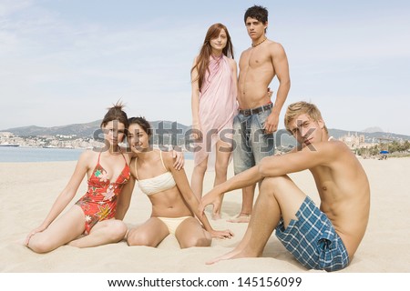 Group of five friends standing on a beach with a blue sky and sea, posing and looking cool and showing a little attitude, being fashionable and relaxing while on a summer vacation.