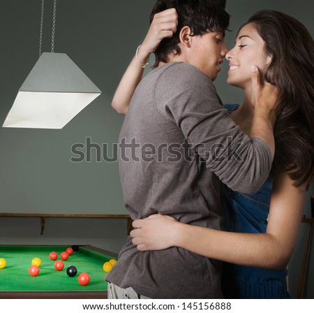 Young couple hugging and kissing with passion in a bar while having a night out in town, playing pool and having fun, interior.