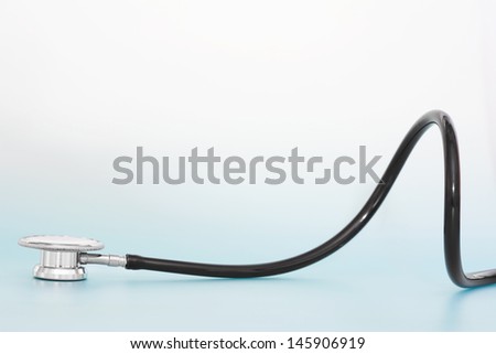 Close up profile view of part of a doctors stethoscope laying down and curling isolated against a clean blue plain background with space above it.