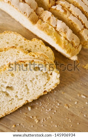 Over head close up view of a loaf of rustic bread sliced in long slices on a kitchen traditional wooden chopping board.
