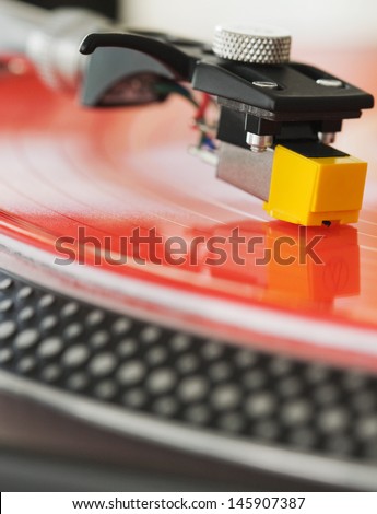 Close up detail view of a dj turntable deck and needle playing music on a red vinyl disc in a nightclub.