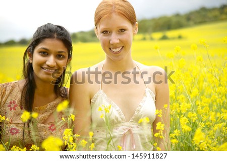 Two teenager girls friends relaxing together on a large yellow flowers field during a summer vacation in the countryside on a sunny day.