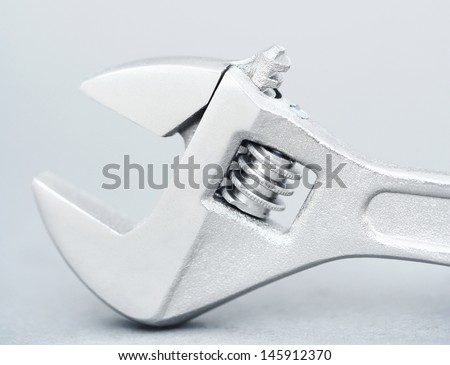 Close up detail view of an open ended silver metallic wrench spanner isolated against a silvery blue grey background.