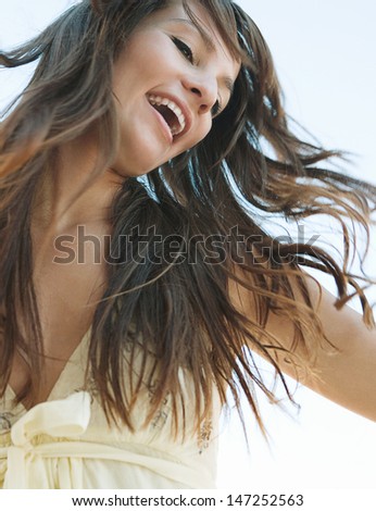 Joyful young woman flicking her hair in the air against a blue sky, smiling and feeling joyful and free and having fun during a sunny day.