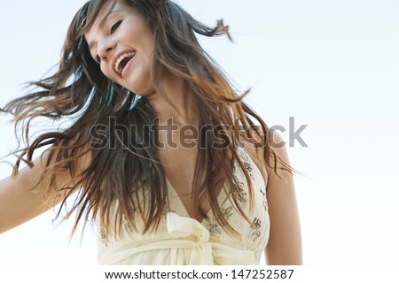 Joyful Young Woman Flicking Her Hair In The Air Against A Blue Sky, Smiling And Feeling Joyful And Free And Having Fun During A Sunny Day.