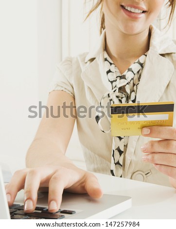 Close up detail of a smart young woman holding a credit card in her hand while making a payment and shopping on the internet using a laptop computer at home.