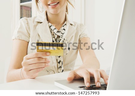 Close up detail of a smart young woman holding a credit card in her hand while making a payment and shopping on the internet using a laptop computer at home.