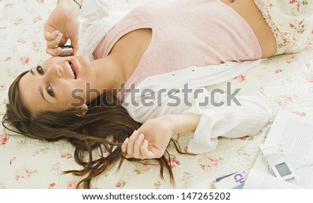 Over head view of a beautiful teenager relaxing and laying down on her bed in her bedroom at home, using a mobile phone to have a conversation with friends.