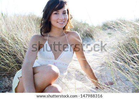 Close up portrait of an attractive young woman relaxing on a beach sand dunes while on vacation, smiling and relaxing during a sunny day.