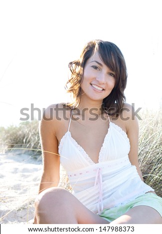 Attractive young woman relaxing on a beach sand dunes while on vacation, smiling and relaxing during a sunny day.