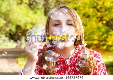 Close up portrait of a teenager playing games and blowing soap bubbles up in the air while in a natural park during a fall autumn sunny day, outdoors.