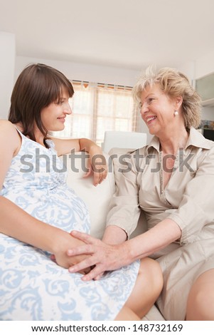 Pregnant mother and grand mother to be sharing a special moment while talking and being proud, sitting at home and holding hands with excitement.