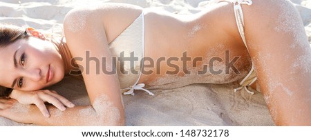 Horizontal view of an attractive young woman laying down and lounging on a white sand fine beach wearing a luxury sexy sequins bikini during the sunset on vacation, outdoors.