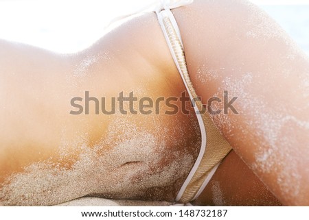 Middle section of a woman body covered in white fine sand while laying down on a beach wearing a luxury sequins bikini with sexy curves, relaxing on vacation,  faceless view.