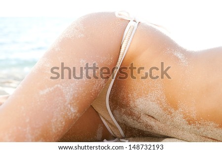 Middle section of a woman body covered in white fine sand while laying down on a beach wearing a luxury sequins bikini with sexy curves, relaxing on vacation,  faceless view.