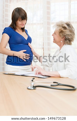 Portrait of an attractive pregnant woman visiting her gynecologist specialist doctor and having a conversation during an appointment at a hospital medical room, indoors.