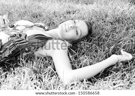 Black and white portrait view of an attractive woman laying on textured green grass listening to music with her mp3 player and smiling joyfully during a summer day outdoors.