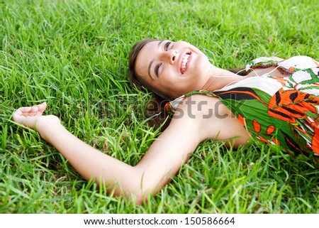 Side portrait view of an attractive young woman laying down on textured green grass listening to music with her mp3 player and smiling joyfully during a summer day outdoors.