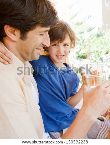 Dad and young son sitting together at a table in a home porch garden outdoors drinking water and enjoying a sunny day while on vacation.