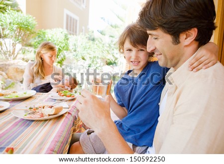 Family of four gathering around a table with food in a home porch garden outdoors with mother, father, baby girl, and a young boy drinking water with dad.