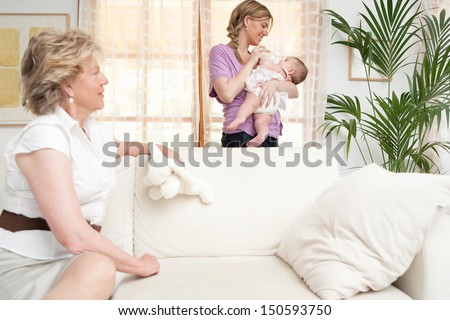 Mother, grandmother and new baby daughter their living room at home relaxing and feeding the baby with a milk bottle. Home interior.